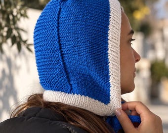 May include: A vibrant blue knitted hood featuring a contrasting white ribbed trim along the face opening. The headwear is constructed with a textured stitch pattern and includes blue ties at the neck to secure the hood in place around the head.