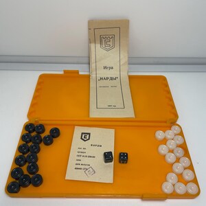 May include: An open orange backgammon set with black and white game pieces, two dice, and printed instructions. The set includes a paper with Cyrillic text and a logo.