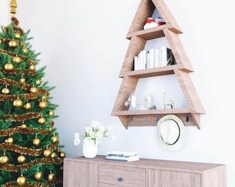 May include: A wooden Christmas tree-shaped shelf with three tiers, holding books, decorations, and a hat. The shelf is mounted on a white wall, next to a decorated Christmas tree and a wooden cabinet. The text "WOODCRAFTPLANS" is visible.