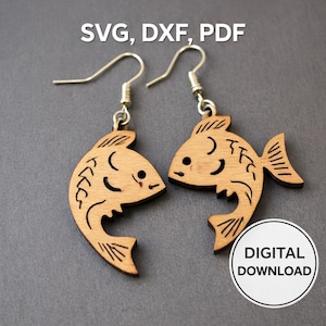 May include: A pair of wooden fish earrings with silver hooks. The earrings are light brown and feature etched details such as fins, scales, and a smiling face. The image also includes the text "SVG, DXF, PDF" and "DIGITAL DOWNLOAD".