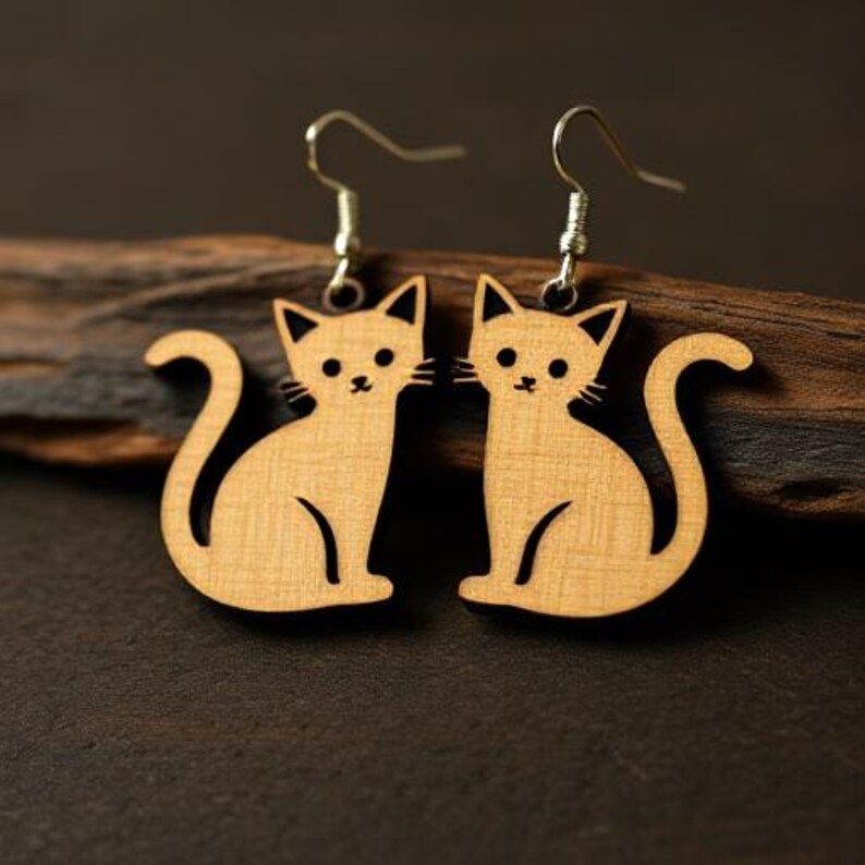 May include: A pair of wooden cat-shaped earrings. The earrings are light brown with black details for the eyes, nose, and mouth. The cat's tail is curled. The earrings hang from silver-colored hooks.