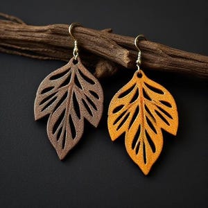 May include: Two leaf-shaped earrings with gold-colored hooks. One earring is brown, the other is orange. The earrings are made of a textured material and are set against a dark background with a piece of wood.