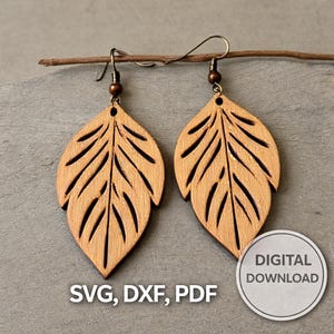 May include: Wooden leaf earrings with a natural wood grain. The earrings feature detailed vein patterns and hang from bronze-coloured ear wires. The image includes the text "SVG, DXF, PDF" and a "DIGITAL DOWNLOAD" badge.