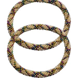 Puede incluir: Dos pulseras de cuentas de color crema con un diseño en espiral. Los bordes de las pulseras están decorados con pequeñas cuentas iridiscentes en tonos morado, verde y dorado. Las pulseras se muestran sobre un fondo blanco.
