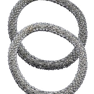 May include: Two silver beaded bracelets. The bracelets are made of small, shiny beads, creating a textured surface. The beads are a mix of silver and clear, giving them a shimmering appearance. The bracelets are circular in shape.