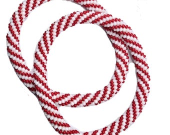 May include: Two beaded bracelets with a spiral design. The bracelets are made of small red and white beads, creating a candy cane-like pattern. The bracelets are circular and appear to be handmade.