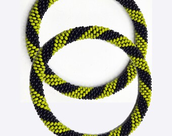 May include: Two beaded bracelets. Each bracelet is a spiral of black and lime green beads. The bracelets are circular and rest on a white background. The beads are small and evenly spaced, creating a textured appearance.