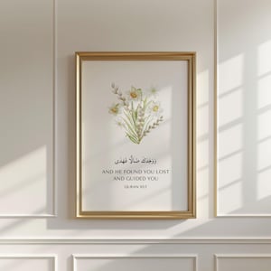 May include: A framed wall art print featuring a watercolor illustration of white and yellow daffodils with green stems. Below the flowers, the text reads in Arabic script, followed by the English text: AND HE FOUND YOU LOST AND GUIDED YOU QURAN 93:7.