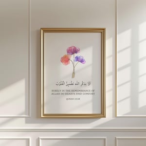 May include: A framed wall art print featuring a watercolor illustration of three flowers in shades of pink, orange, and purple. Below the flowers, the text reads: "أَلَا بِذِكْرِ اللَّهِ تَطْمَئِنُّ الْقُلُوبُ SURELY IN THE REMEMBRANCE OF ALLAH DO HEARTS FIND COMFORT QURAN 13:28."
