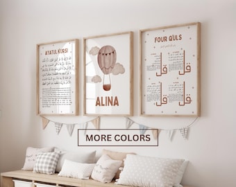 May include: Three framed wall art prints in light wood frames. The left print features Ayatul Kursi text, the centre print shows a hot air balloon with the name ALINA, and the right print displays Four Quls text. A fabric bunting hangs below.