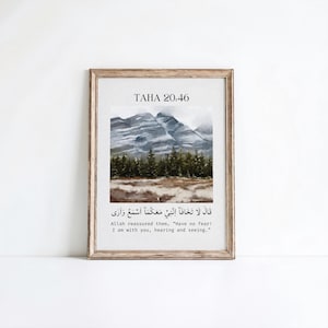 Puede incluir: Impresión artística enmarcada con un paisaje de acuarela de montañas y árboles. La impresión incluye texto árabe y la traducción al inglés: "¡No temas! Estoy contigo, escuchando y viendo." El marco es de color marrón claro.