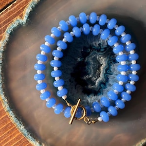 Puede incluir: Un collar de doble cadena con cuentas de color azul claro y blanco y un cierre de palanca dorado.