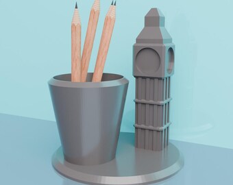 May include: A gray pencil holder shaped like Big Ben with a gray cup for pencils. Three wooden pencils are in the cup.