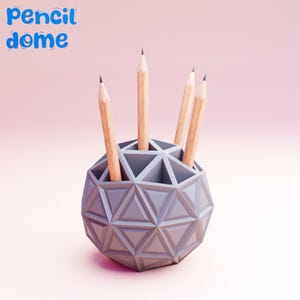 May include: A gray geometric pencil holder shaped like a dome with four pencils sticking out of it. The text "pencil dome" is written in blue letters on a pink background.