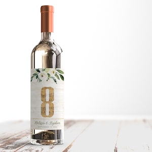 May include: A white wine bottle with a personalized wedding label. The label features a floral design with white flowers and green leaves. The label also includes the text "Melissa & Stephen" and the date "September 13, 2020". The bottle is labeled with the number "8".