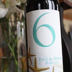 May include: A wine bottle with a white label featuring a teal number six, two starfish, and the text "Paul & Maria 6.12.12".