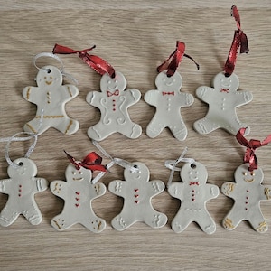 Peut inclure: Ensemble de huit décorations en forme de bonhomme en pain d'épices en céramique blanche. Chaque ornement est orné d'un ruban rouge pour la suspension et décoré d'accents rouges et dorés. Certains ont des nœuds papillon.