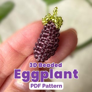May include: A handcrafted, 3D beaded eggplant in shades of purple and green. The miniature vegetable is made of small beads, with a green beaded stem. Text on the image reads "3D Beaded Eggplant PDF Pattern".
