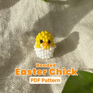 Peut inclure: Un poussin de Pâques perlé, composé de perles jaunes et blanches, est présenté sur une surface texturée. Le poussin a des yeux noirs et un bec orange, sortant d'une coquille d'œuf perlée blanche. Le texte "Beaded Easter Chick PDF Pattern" est inclus.
