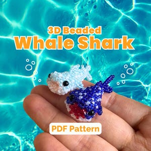 May include: Two beaded whale shark figures, one light blue and one dark blue, are held in a hand. The light blue shark has white accents, while the dark blue shark has red and white accents. The text "3D Beaded Whale Shark" and "PDF Pattern" are displayed.