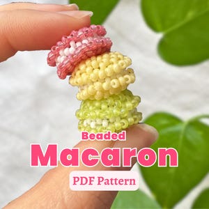May include: A stack of three beaded macarons in pink, yellow, and green, held between fingers. The top macaron is pink with white beads, the middle is yellow, and the bottom is green. Text on the image reads "Beaded Macaron PDF Pattern".