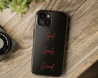 Op de afbeelding: Zwarte telefoonhoes met een rode inscriptie die "God, Doelen, Grind" luidt.