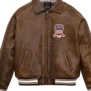 Puede incluir: Chaqueta de cuero marr&oacute;n de estilo bomber. Tiene cuello, cierre de cremallera y dos bolsillos delanteros. Un parche bordado con un escudo est&aacute; en el pecho. Los pu&ntilde;os y el dobladillo tienen un patr&oacute;n de rayas.
