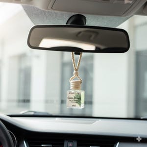 May include: A car air freshener hanging from a rearview mirror. The clear glass bottle has a wooden cap and a beige string. The label reads "Calm Down" and "Car Air Freshener Oil Diffuser 10ml". The car interior is visible in the background.