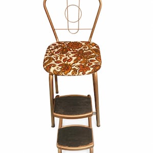 May include: A metal step stool chair with a bronze-toned frame and a seat upholstered in a cream fabric featuring an orange and brown floral pattern. The unit includes two retractable steps with black, textured, non-slip surfaces for climbing.