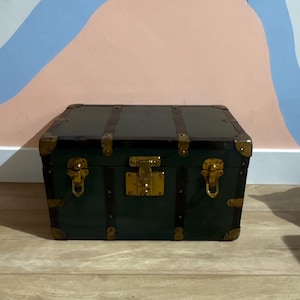 May include: A dark green rectangular storage trunk featuring dark brown leather-like straps and polished gold-tone metal hardware. The chest includes reinforced metal corner protectors, two side latches, and a central locking mechanism on the front.