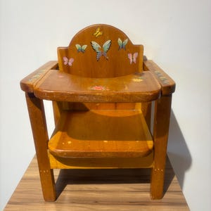以下が含まれることがあります： 天然仕上げの木製ハイチェア。小さな座席、フットレスト、さまざまな色の蝶のデカールで装飾された背もたれが特徴です。椅子は子供向けに設計されています。