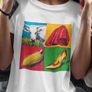 May include: White t-shirt with a colorful four-square design featuring a cow, a red cape, an ear of corn, and a gold high heel shoe.