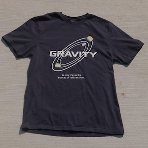 May include: Dark blue t-shirt featuring the word "GRAVITY" in white, with a diagram of planets in orbit. The text "is my favourite force of attraction" is below the diagram. The shirt is made of a soft material.