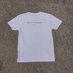 May include: A white short-sleeved t-shirt featuring the text AN AUTHENTIC WAY OF LIVING printed in a rainbow gradient across the chest, with the smaller text Phdrevolution printed directly underneath in a simple black font.