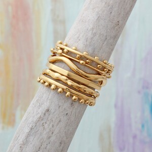 May include: A set of six gold stacking rings with different textures and designs. The rings are stacked on top of each other and are made of a smooth, shiny metal.