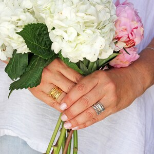 May include: A bouquet of white hydrangeas and pink peonies held by hands wearing gold and silver stacking rings.