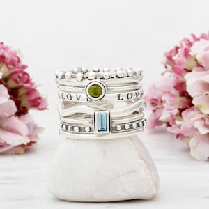 May include: A stack of silver rings with a green and blue gemstone. The rings are decorated with small beads and the word "LOVE" is engraved on two of the rings.