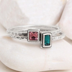 May include: Two silver rings with textured bands. One ring features a square pink gemstone, and the other ring features a rectangular teal gemstone.