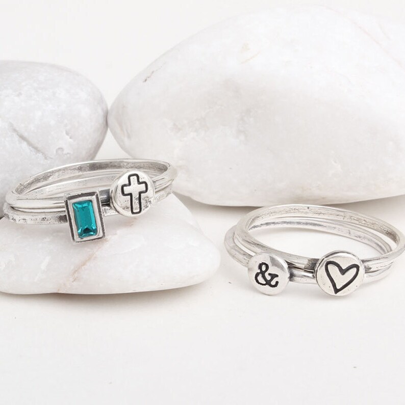 Pu&ograve; includere: Tre anelli d'argento con design diversi. Un anello ha una pietra turchese, un altro ha una croce e il terzo ha una e commerciale e un cuore.