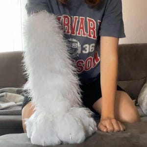 May include: A long, white, faux fur sleeve or arm covering with a thick, shaggy texture. The accessory extends from the wrist area up to the upper arm, featuring dense, soft white synthetic fibres that create a voluminous, plush appearance.