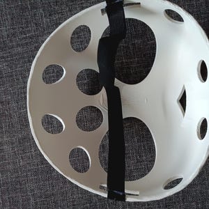 以下が含まれることがあります： 黒い調節可能なストラップが付いた白いプラスチック製のホッケーマスク。マスクには複数の丸い穴とダイヤモンド型の開口部があります。