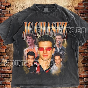 Peut inclure: T-shirt gris foncé avec un collage d'images d'un groupe de musique et le texte "JC CHASEZ" en orange et blanc. Le t-shirt porte également le texte "SOUTH KREO" en blanc. Le t-shirt a un aspect vintage et vieilli.