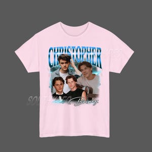 Peut inclure: T-shirt rose clair avec un collage de quatre images d'une personne, avec le texte "CHRISTOPHER" en bleu et le nom "Briney" en cursive. Le t-shirt a un col rond et des manches courtes.