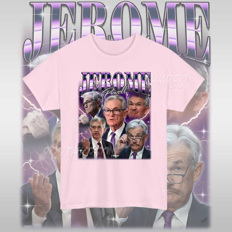 May include: Pink t-shirt with a graphic print of Jerome Powell, the chairman of the Federal Reserve, in a retro style. The graphic features Powell's face surrounded by lightning bolts and the text "JEROME Powell" in a bold, purple font.