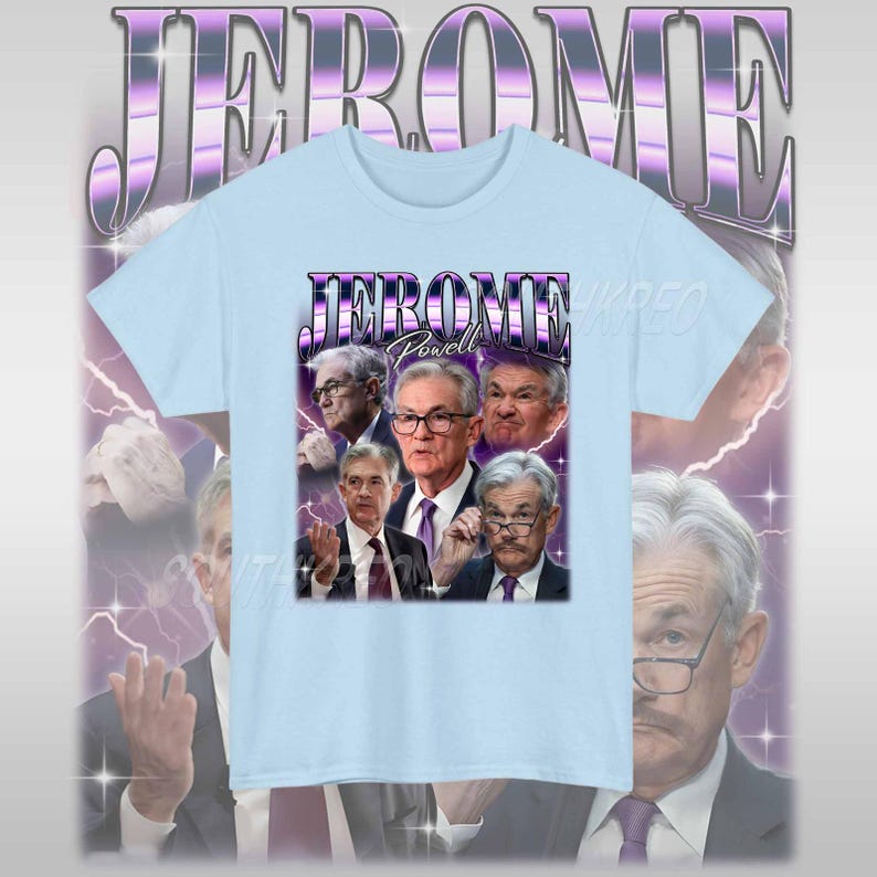 May include: Light blue t-shirt with a graphic print of Jerome Powell, the chairman of the Federal Reserve, in a retro style. The text "JEROME Powell" is printed in purple on the shirt.