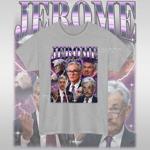 May include: A grey t-shirt with a graphic print of Jerome Powell, the chairman of the Federal Reserve, surrounded by other men. The text "Jerome Powell" is printed in a bold, white font.