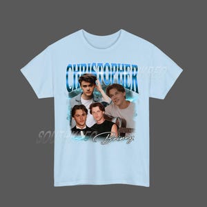 Peut inclure: T-shirt bleu clair avec un collage de quatre images d'une personne. Le nom "CHRISTOPHER" est &eacute;crit en bleu, dans une police stylis&eacute;e en haut. Le nom "Briney" est &eacute;crit en cursive en bas.