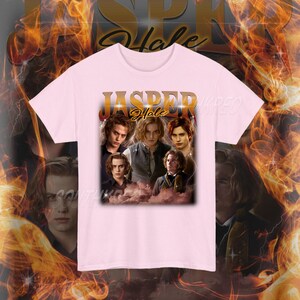 K&ouml;nnte beinhalten: Hellrosa T-Shirt mit einem Aufdruck, der mehrere Gesichter und den Text "JASPER Hale" in Gold zeigt. Das Design ist eine Collage von Bildern. Das T-Shirt hat einen Rundhalsausschnitt.