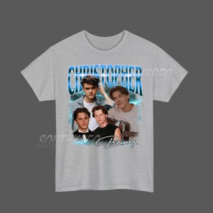 Peut inclure: Un t-shirt gris clair avec un imprim&eacute; de quatre jeunes hommes et le nom "Christopher" en bleu. Le mot "Briney" est &eacute;crit en cursive en dessous des images. Le t-shirt a des manches courtes.