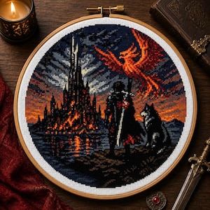 Può includere: Un ricamo a punto croce circolare in un telaio di legno che mostra la sagoma scura di una figura con una spada e un lupo davanti a un alto castello luminoso al tramonto, con una grande e vivace fenice arancione che vola nel cielo.